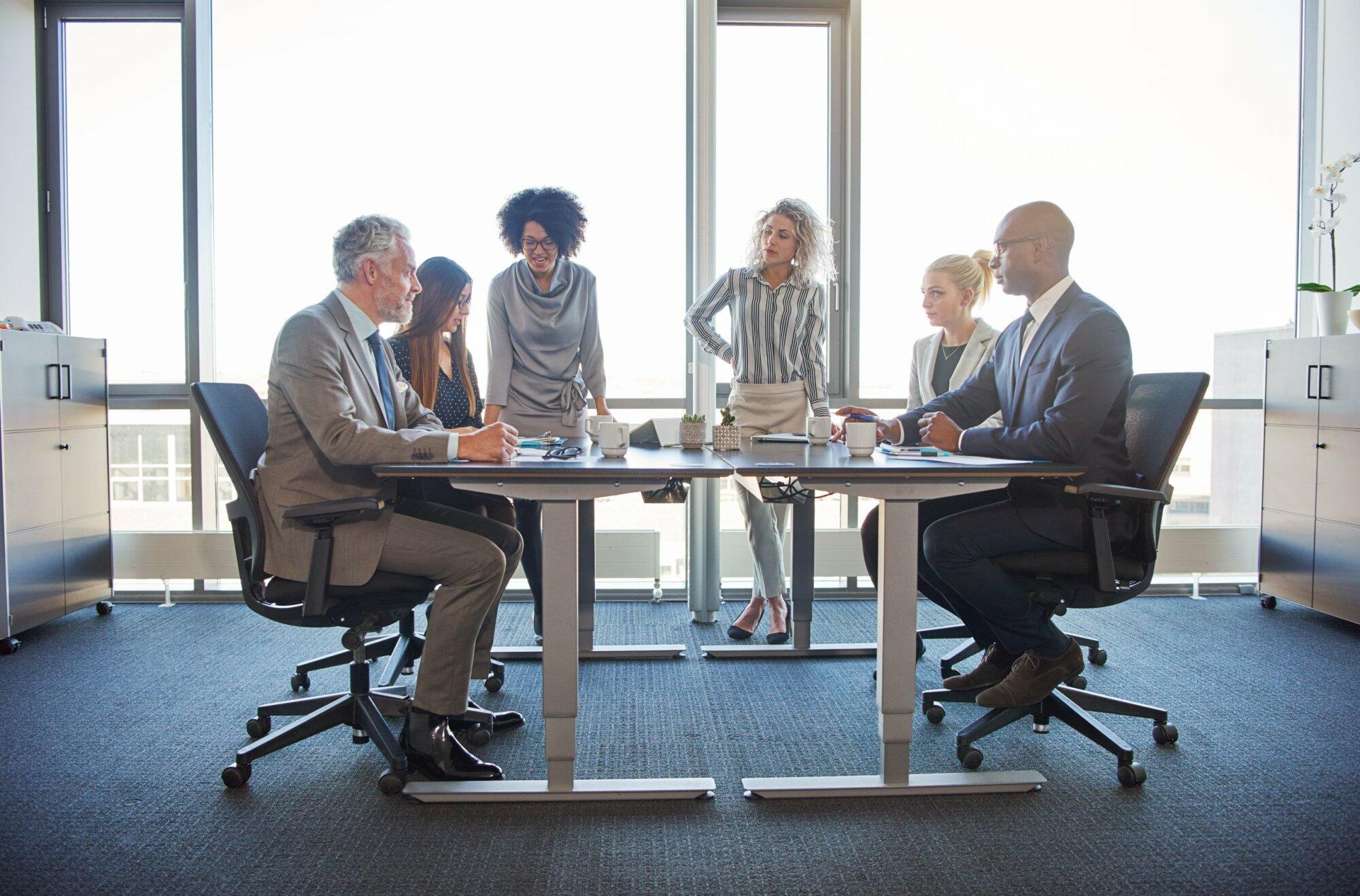 Diverse group of corporate colleagues talking together around a table during a meeting in a bright modern office